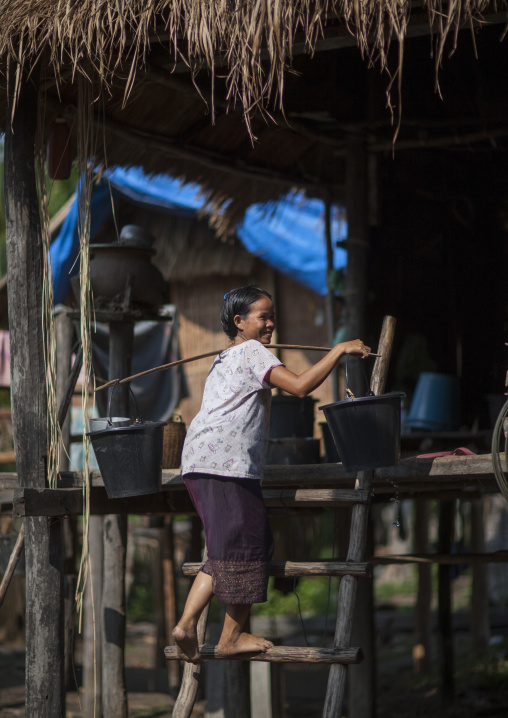 Bru minority woman carrying water in her house, Phonsaad, Laos