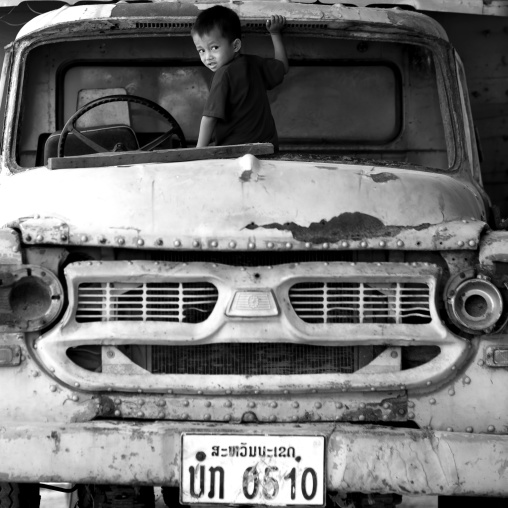 Boy playing in an old car, Thakhek, Laos