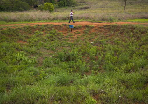 Man passing in front of a bomb crater at plain of jars, Phonsavan, Laos