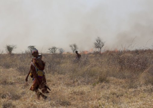 San Woman With Her Baby Passing By A Fire In The Bush, Namibia