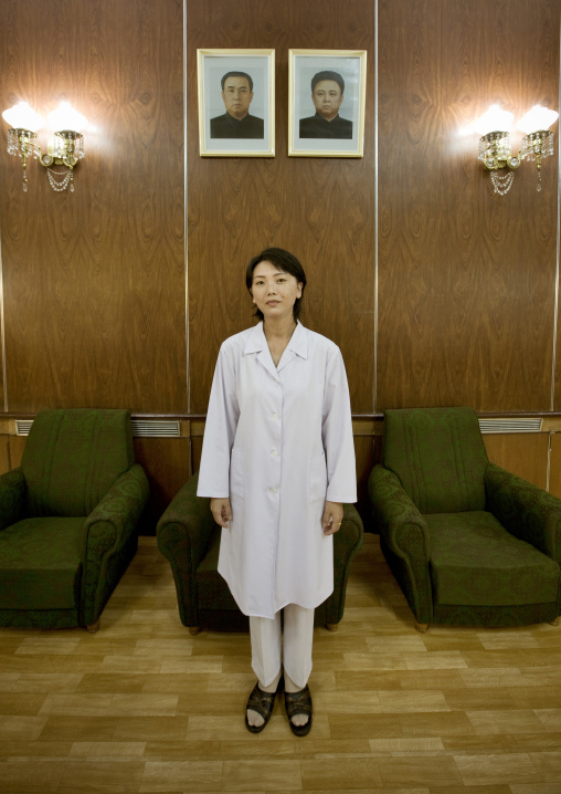 North Korean doctor at the maternity posing below the official portraits of the Dear Leaders, Pyongan Province, Pyongyang, North Korea