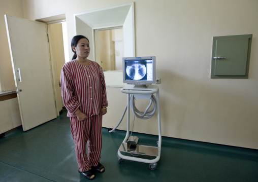 North Korean woman acting like a patient for the tourists in front of an x ray machine in maternity hospital, Pyongan Province, Pyongyang, North Korea