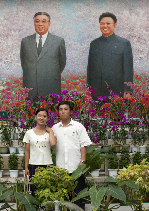 North Korean couple posing in front of the Dear Leaders fresco at the international Kimilsungia and Kimjongilia festival, Pyongan Province, Pyongyang, North Korea