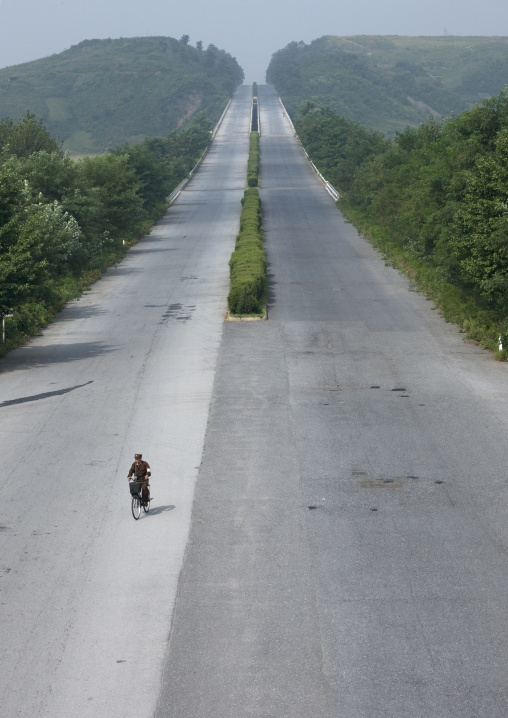 North Korean soldier riding a bicycle on an empty highway, Pyongan Province, Pyongyang, North Korea
