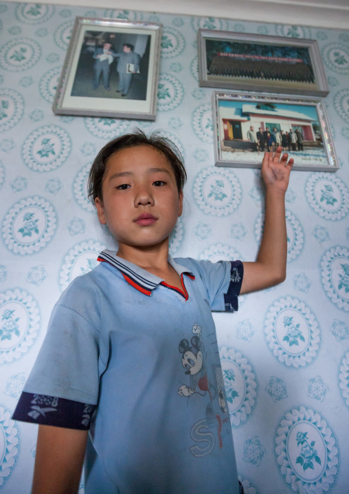North Korean girl posing below the portraits of the Dear Leaders inside her home, Kangwon Province, Chonsam Cooperative Farm, North Korea