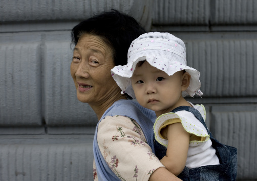 North Korean Grand mother carrying a toddler girl on her back, Pyongan Province, Pyongyang, North Korea