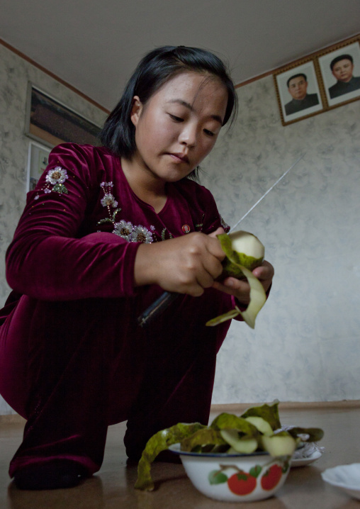 North Korean woman peeling pears below the official portraits of the Dear Leaders, South Hamgyong Province, Hamhung, North Korea