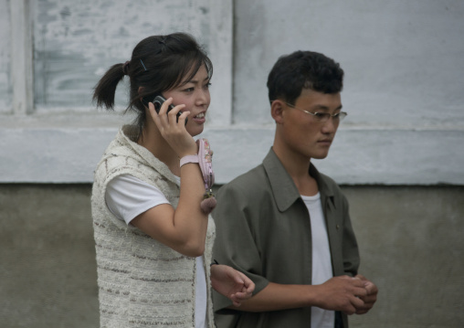 Young North Korean woman using a cell phone and walking with a young man in the street, Kangwon Province, Wonsan, North Korea