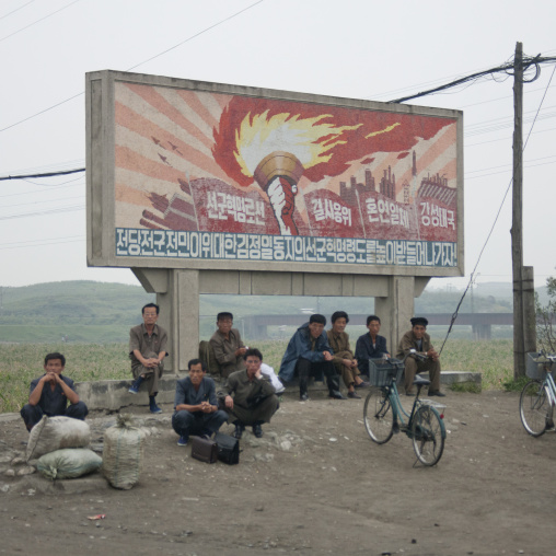 North Korean workers having a rest below a juch tower flame billboard, South Hamgyong Province, Hamhung, North Korea