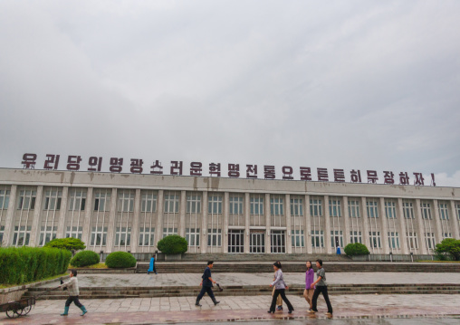 North Korean people passing in front of a building with propaganda slogan on the top saying let us arm ourselves firmly with the glorious revolutionary tradition of our party!, South Hamgyong