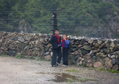 Two North Korean boys standing next to a high fence on a road, North Hamgyong Province, Jung Pyong Ri, North Korea