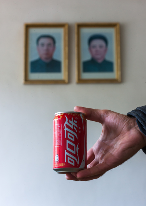 Can of North Korean coca cola in front of the portraits of Kim il Jong and Kim Jong il, Ryanggang Province, Samjiyon, North Korea