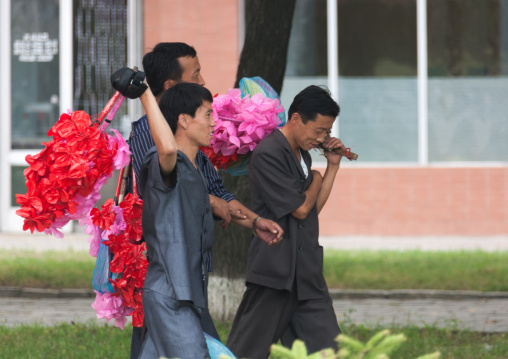 North Korean men with plastic flowers going celebrate the day of the foundation of the republic, Pyongan Province, Pyongyang, North Korea