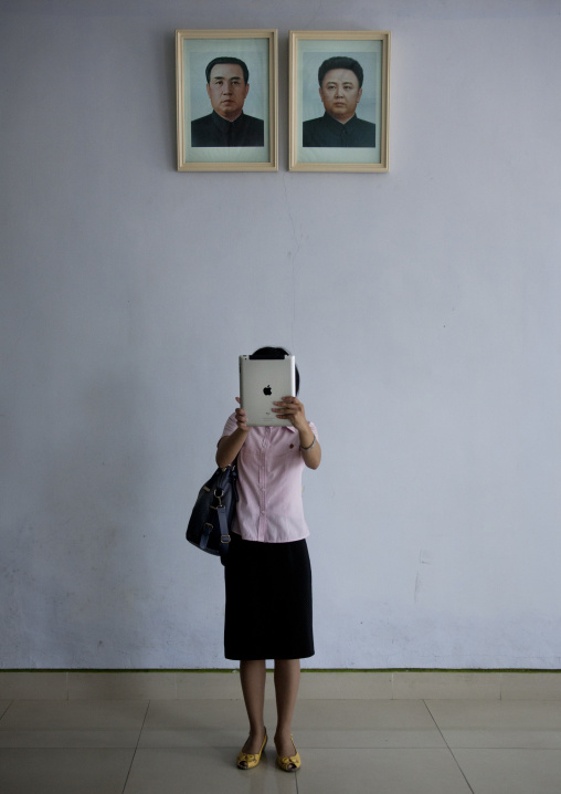 North Korean woman with an ipad in front of the official portraits of Kim il Sung and Kim Jong il, North Hwanghae Province, Panmunjom, North Korea