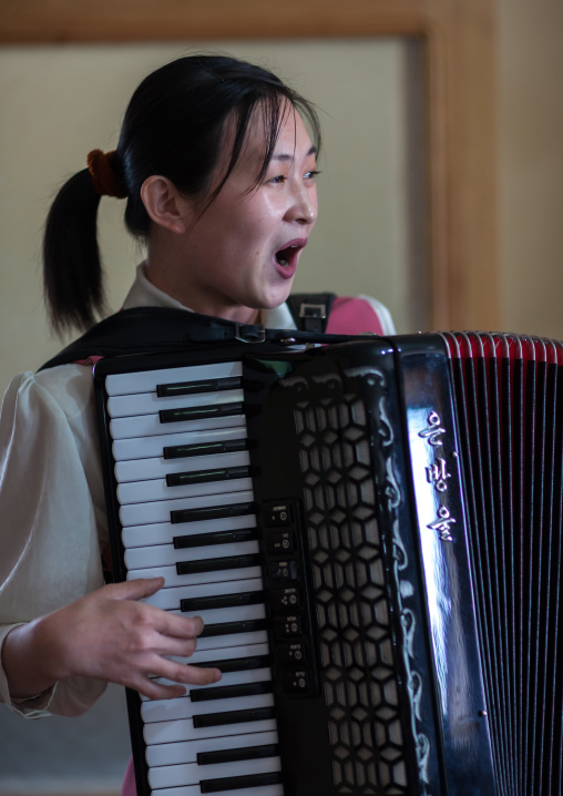 North Korean waitress in a restaurant singing and playing accordion, Pyongan Province, Pyongyang, North Korea