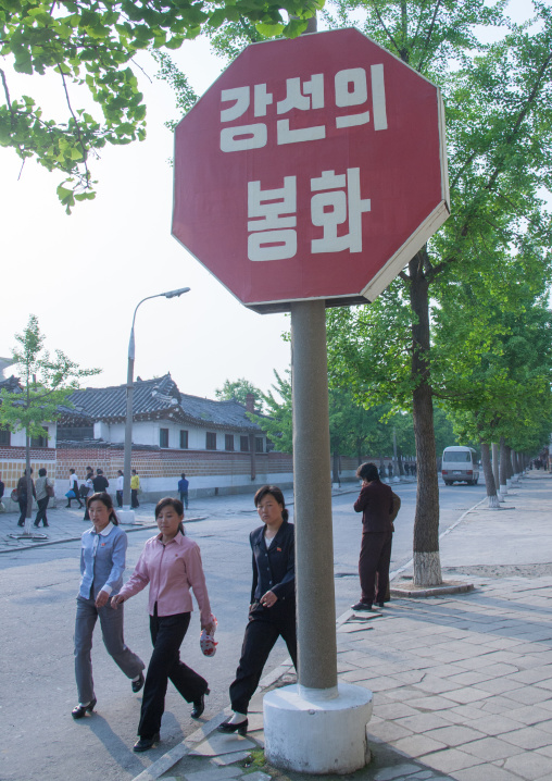 North Korean women passing by red propaganda billboard saying flame of kangson, North Hwanghae Province, Kaesong, North Korea