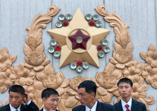 North Korean men under the rain in Kumsusan memorial palace posing in front of the supreme commander of the Korean people's army logo, Pyongan Province, Pyongyang, North Korea