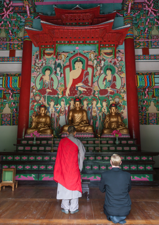Monk and tourist praying in front of the altar of Kwangbok temple, Pyongan Province, Pyongyang, North Korea