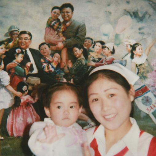 Polaroid of a smiling nurse with a child in front of a poster with the Dear Leaders, South Pyongan Province, Nampo, North Korea