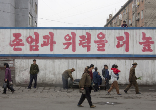North Korean people walikng in the street in front of a propaganda billboard, South Pyongan Province, Nampo, North Korea