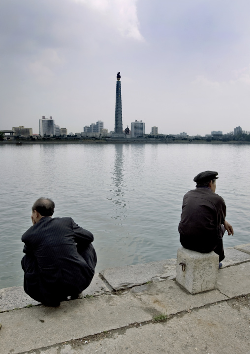 North Korean men sit in front of the Taedong river with the Juche tower in the background, Pyongan Province, Pyongyang, North Korea