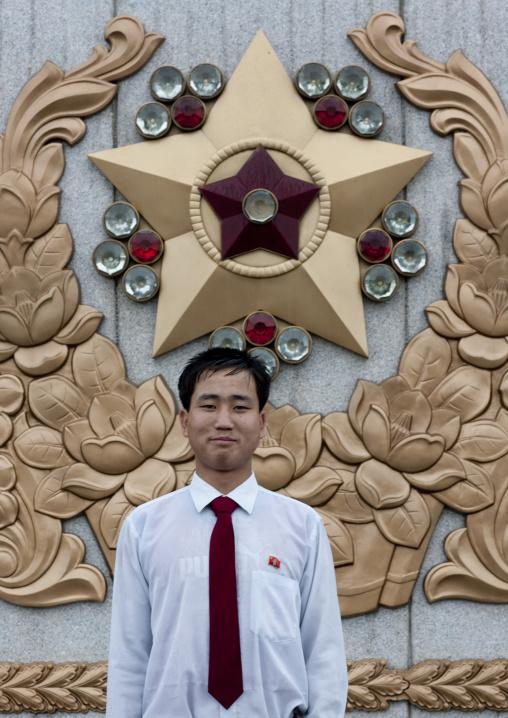 North Korean man under the rain in Kumsusan memorial palace posing in front of the supreme commander of the Korean people's army logo, Pyongan Province, Pyongyang, North Korea