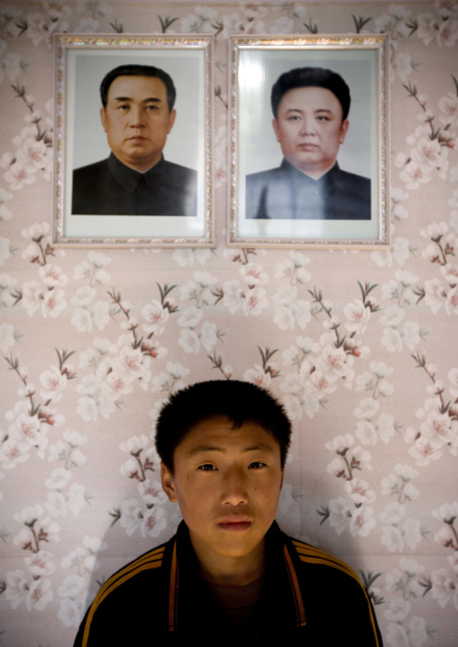 North Korean boy posing below the portraits of the Dear Leaders in his home, Kangwon Province, Chonsam Cooperative Farm, North Korea