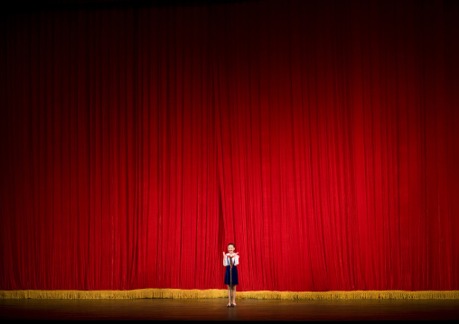 North Korean girl in front of a red curtain on the stage of Mangyongdae theatre, Pyongan Province, Pyongyang, North Korea
