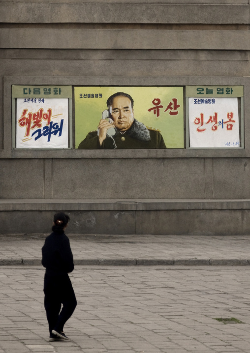 North Korean woman looking a movie poster with a military man on the phone, Pyongan Province, Pyongyang, North Korea