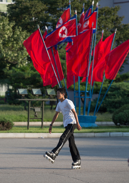 North Korean boy roller skating in front of red flags, Pyongan Province, Pyongyang, North Korea