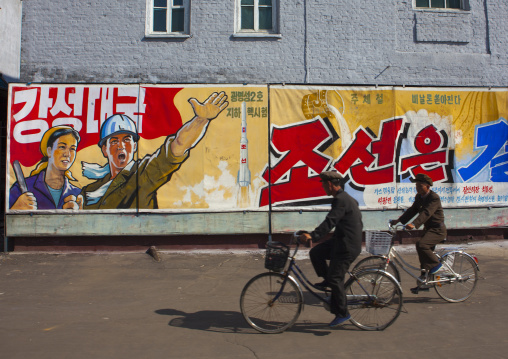 North Korean men riding bicycles in front of propaganda billboards in Hungnam nitrogen fertilizer plant, South Hamgyong Province, Hamhung, North Korea