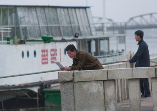North Korean man reading a newspaper in front of a boat, Pyongan Province, Pyongyang, North Korea