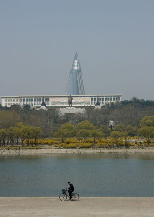 Man on a bike with Ryugyong hotel and Mansudae Grand monument in the background, Pyongan Province, Pyongyang, North Korea