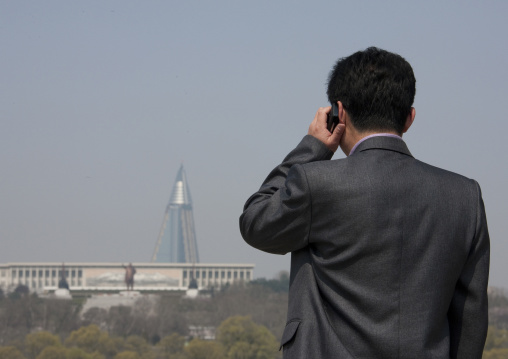 North Korean man calling with his mobile in front of the pyramid-shaped Ryugyong hotel
, Pyongan Province, Pyongyang, North Korea