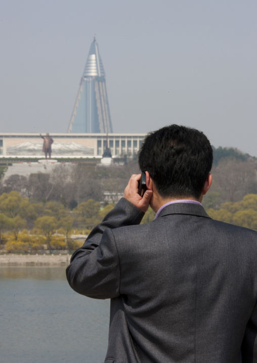 North Korean man calling with his mobile in front of the pyramid-shaped Ryugyong hotel, Pyongan Province, Pyongyang, North Korea
