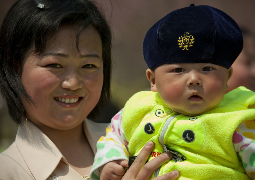 North Korean mother holding her baby who wears a beret in her arms, Pyongan Province, Pyongyang, North Korea