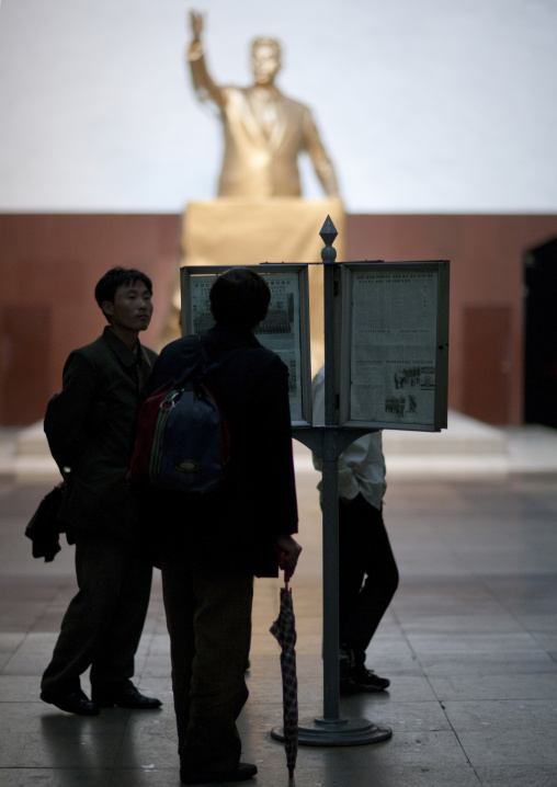 North Korean people reading a newspaper in Kaeson metro station in front of a golden statue of Kim il Sung, Pyongan Province, Pyongyang, North Korea