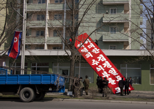 North Korean men setting a propaganda slogan on a red billboard in town, Pyongan Province, Pyongyang, North Korea
