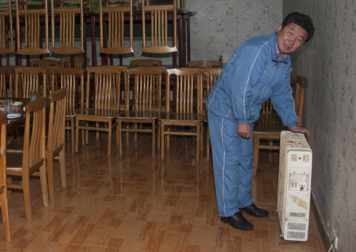 North Korean guide looking for heat in a homestay, North Hamgyong Province, Jung Pyong Ri, North Korea