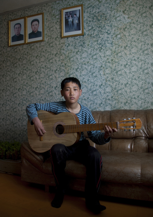 North Korean boy playing guitar in front of the official portraits of the Dear Leaders on the wall, North Hamgyong Province, Jung Pyong Ri, North Korea