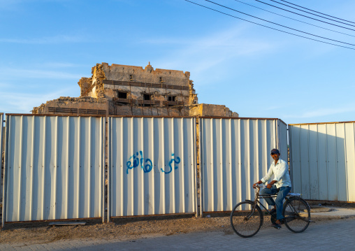 Indian man passing in front of the old palace protected by a fence, Dhofar Governorate, Mirbat, Oman