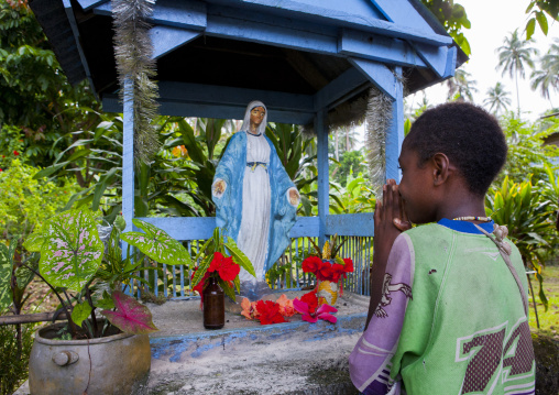 Young girl praying in front of virgin maria statue, New Ireland Province, Langania, Papua New Guinea