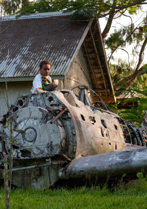 Boy sit on a plane wrecks in the war museum garden, East New Britain Province, Rabaul, Papua New Guinea