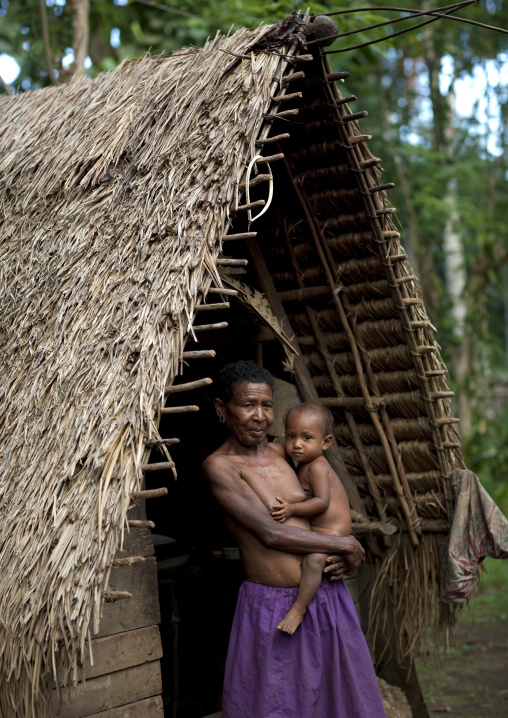 Mother and child in front of an house with thatched roof, Milne Bay Province, Trobriand Island, Papua New Guinea