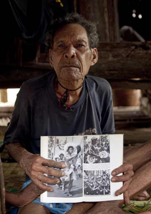 Old man holding an old book with his picture when he was young, Milne Bay Province, Trobriand Island, Papua New Guinea
