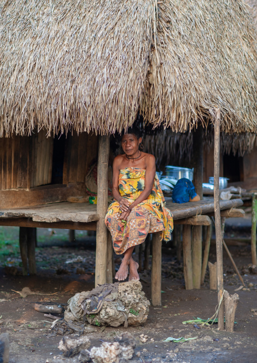 Woman sit under the thatched roof of her house, Milne Bay Province, Trobriand Island, Papua New Guinea