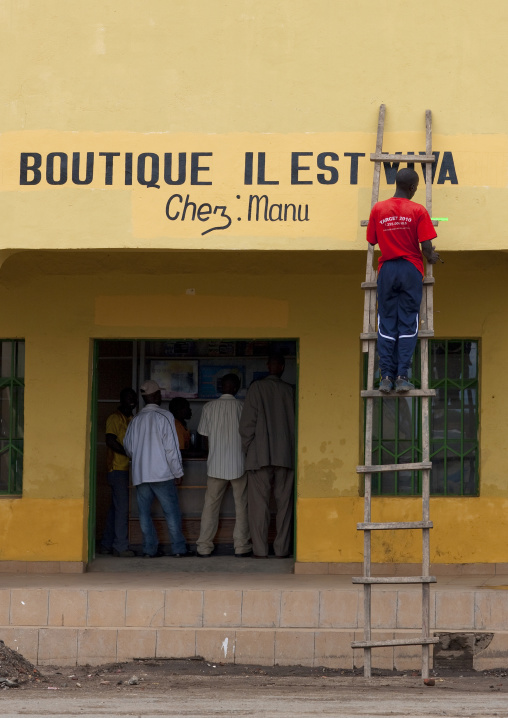 Rwandan man painting his shop wall on a ladder, Lake Kivu, Gisenye, Rwanda