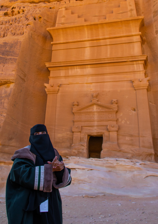 Saudi female guide in front of a tomb in al-Hijr archaeological site in Madain Saleh, Al Madinah Province, Alula, Saudi Arabia