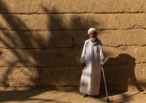 Old saudi man standing in front of a mud house, Najran Province, Najran, Saudi Arabia