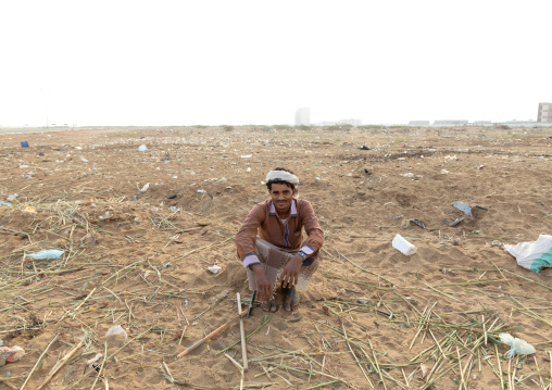Portrait of a man squatting in a field full of wastes, Jizan Province, Sabya, Saudi Arabia
